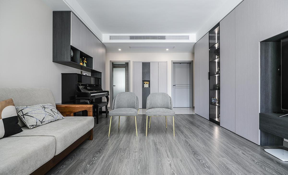 客廳開間很大，電視墻做一排裝飾柜，空間也很寬闊、裝飾柜采用淺灰色門板、淺灰和深灰相互配合，明暗有神，既能儲物又能裝飾、黑色的鋼琴上主做一排，黑白相配的吊柜，原木色沙發框架+淺灰色座墊讓客廳的氛圍年輕起來了。吊頂造型上采用雙眼皮吊頂。地面采用灰色地板。造型和色調上無不給人以簡潔、大氣、時尚的感覺。