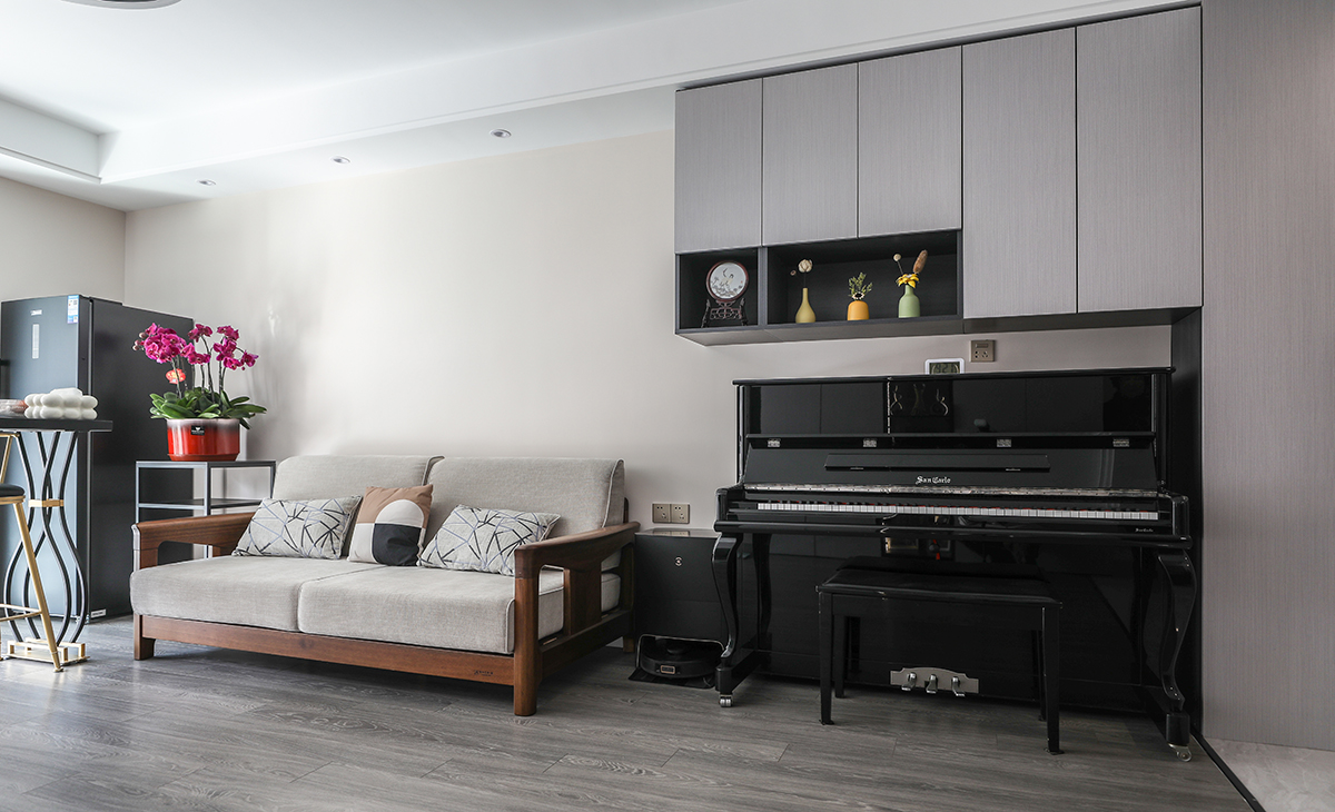 沙發背景刷米色涂料，留白設計，黑白相間的儲物柜和黑色的鋼琴相呼應，色調上用實木沙發米灰色座墊和背景的米色相呼應，和地板相銜接，顯得既大氣又時尚。