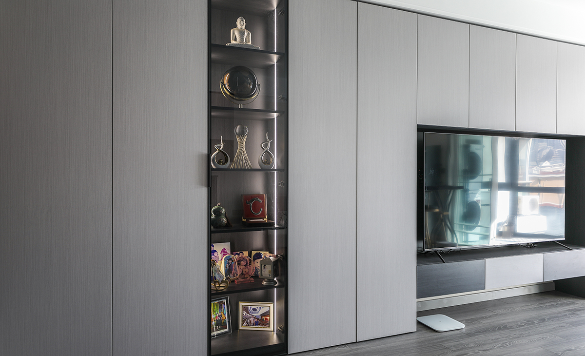 玻璃柜內的裝飾品被層板燈點綴的恰到好處，頂上的射燈作為輔助光為電視墻增加氛圍感，淺灰為主色調，黑色點綴，讓空間不便時尚而且清爽。