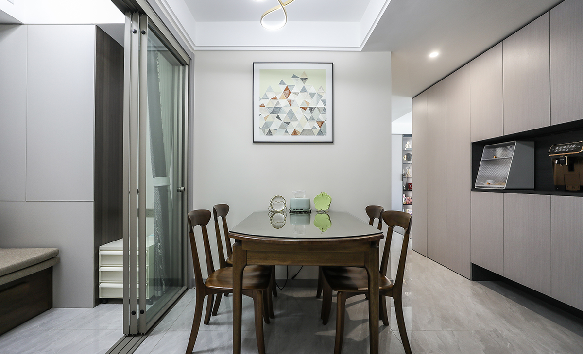餐廳空間比較方正寬敞，雙眼皮圍邊，既實用、又有裝飾功能，墻面一幅裝飾畫把餐廳點綴的很有生機，實木餐桌把用餐氛圍調和的很溫暖，淺灰色地磚很干凈，餐廳側面和臥室之間用移門分隔，色彩和造型上都簡潔大氣。