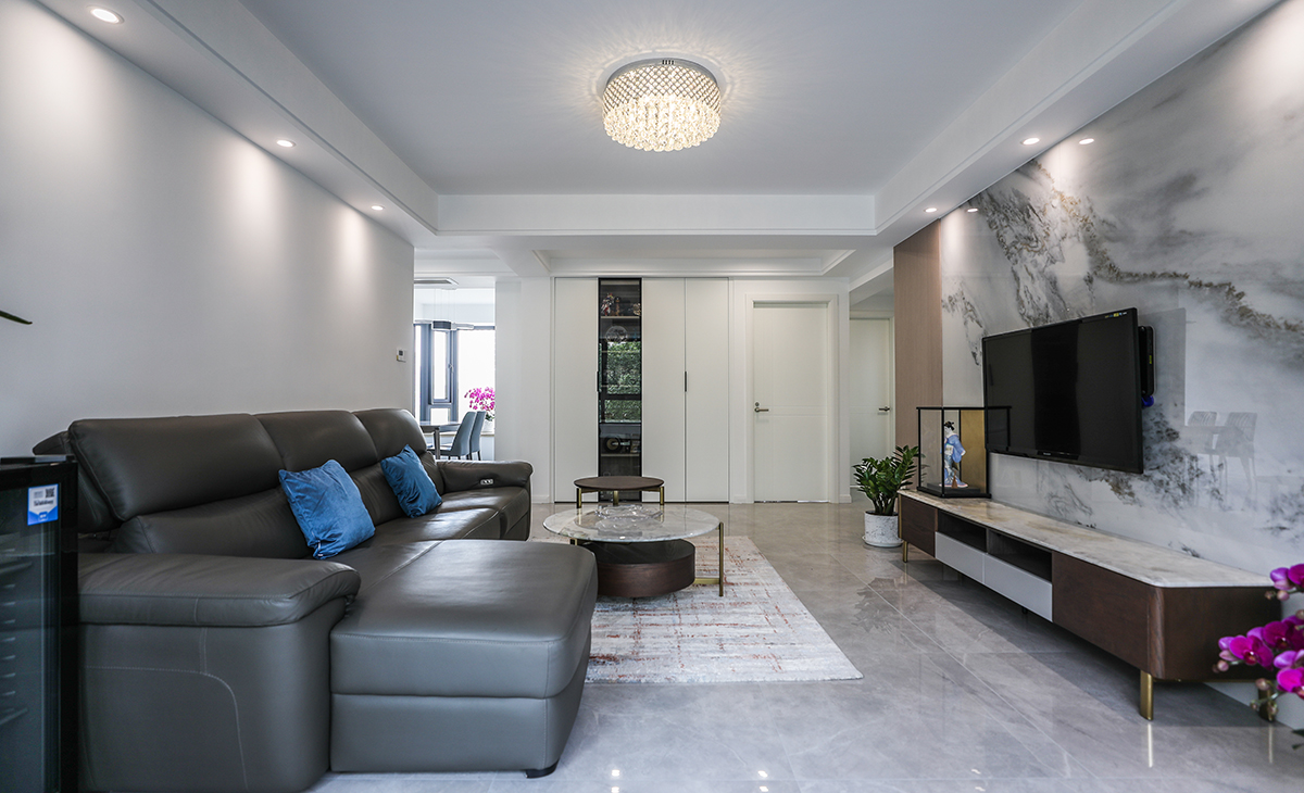 客廳開間很大，電視墻做兩片巖板，兩塊木飾面，淺的巖板和原木色木飾面相互配合，明暗有神，深灰色皮質(zhì)沙發(fā)立刻檔次提高很多，放一組貴妃沙發(fā)，客廳空間也很寬闊。吊頂造型上采用雙眼皮吊頂。地面采用淺灰色地磚。造型和色調(diào)上無不給人以簡潔、大氣、時尚的感覺。