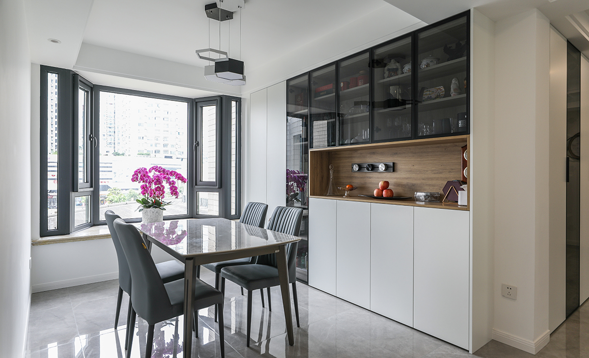 餐廳空間比較方正寬敞，又有一個大飄窗，靠墻做一排裝飾柜，既實(shí)用、又有裝飾功能，原木色框架，極窄邊框玻璃門和白色木門板相呼應(yīng)，巖板餐桌把用餐氛圍調(diào)和的很溫暖，淺灰色地磚很干凈，色彩和造型上都簡潔大氣。