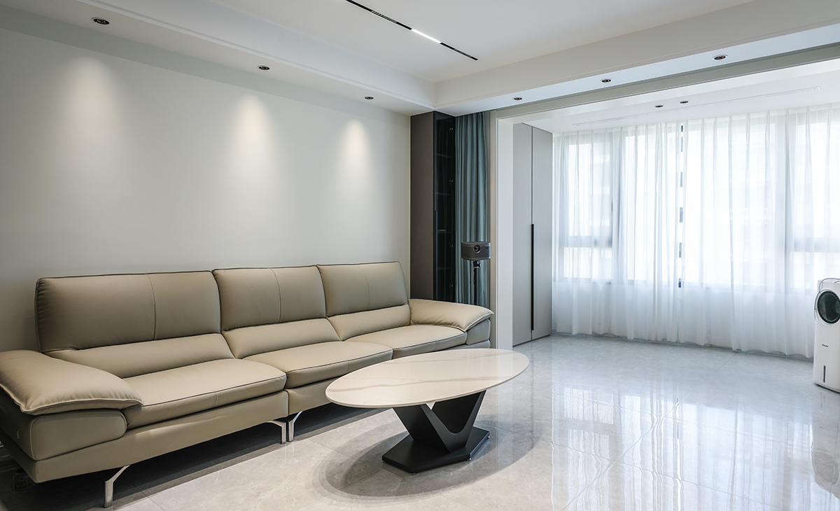 巖板臺面的茶幾襯托出時尚的質感，射燈加上頂面的磁吸軌道燈投射出不同范圍的光源，沙發旁的玻璃柜時尚大氣，典雅的顏色與灰色墻面相得益彰，更與沙發形成落差，極具設計感和居家體驗感。