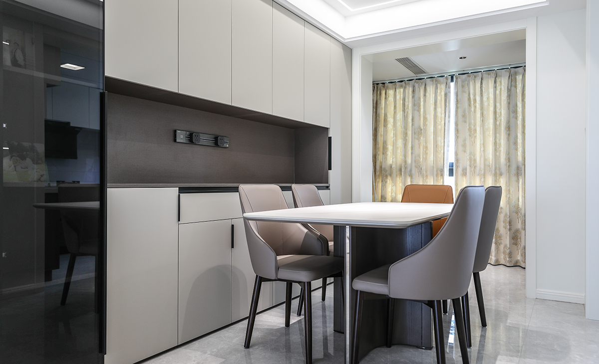 餐廳區域戶型周正，緊鄰小陽臺，空間通透采光好，沿墻滿做一排餐邊柜，實用且高級，增加儲物功能的同時，更為裝飾效果加分，嵌在餐邊柜上的移動排插也解決了客戶的用電剛需，整體色彩以黑白灰為主，造型美觀大氣。