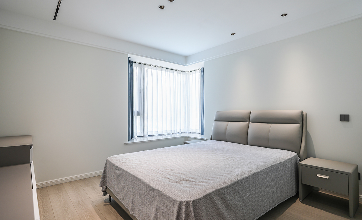 主臥地面鋪以暖灰色地板，衣柜與墻面色彩統一，相得益彰。四周雙眼皮吊頂加上中間拉平無主燈的設計，讓空間顯得尤為寬敞，灰色的床及床頭柜與整個風格進行搭配，渾然一體，整體協調，盡顯主人高端品味。