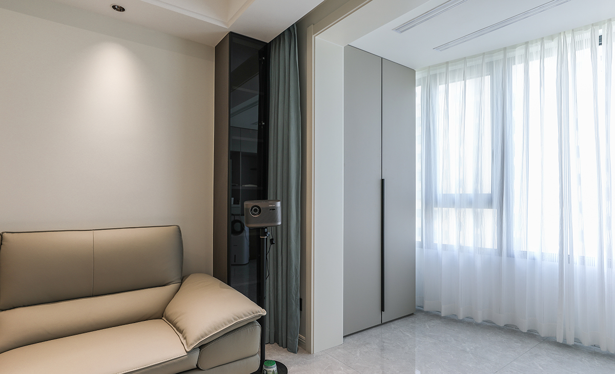 陽臺的頂部暗藏隱形晾衣架，石膏板吊頂之后，頂面平整有序。洗衣機的對面一側，采取全屋定制儲物柜，選用灰色門板加黑色長拉手，一門到頂，整齊又好看。