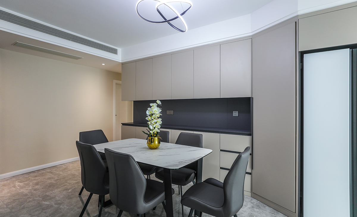 餐廳的餐邊柜加上雙門大冰箱一體合成，灰色柜體板和瓷磚呼應(yīng)，奶咖色柜門板讓整個家庭溫馨起來，超薄巖板餐桌簡約大氣。