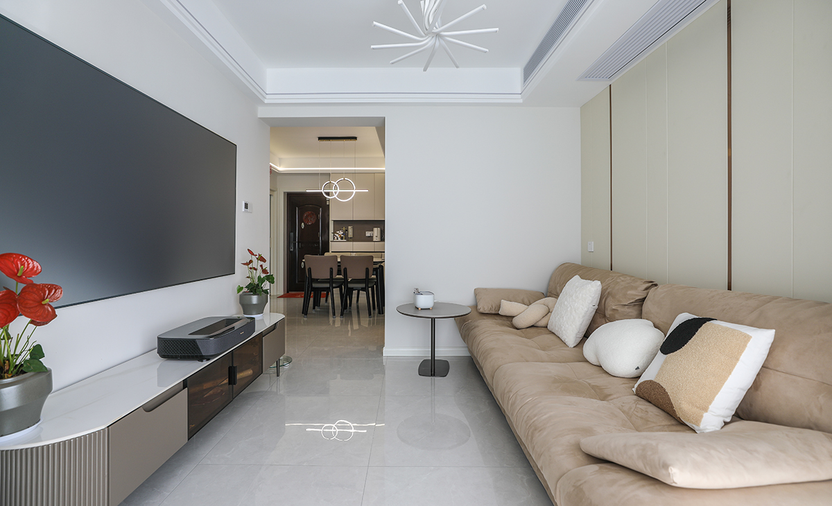 客廳開間并不大，電視墻也并不是很長，所以對于電視墻沒有做過多的裝飾，后期配上65寸的激光電視更顯簡約。暖色調一字型布藝沙發(fā)給冰冷的空間帶來一絲溫暖，吊頂造型上采用雙眼皮吊頂下邊沿嵌入線條燈，增加房屋的層次以及氛圍感。地面采用淺灰色地磚。造型和色調上無不給人以簡潔、大氣、時尚的感覺。