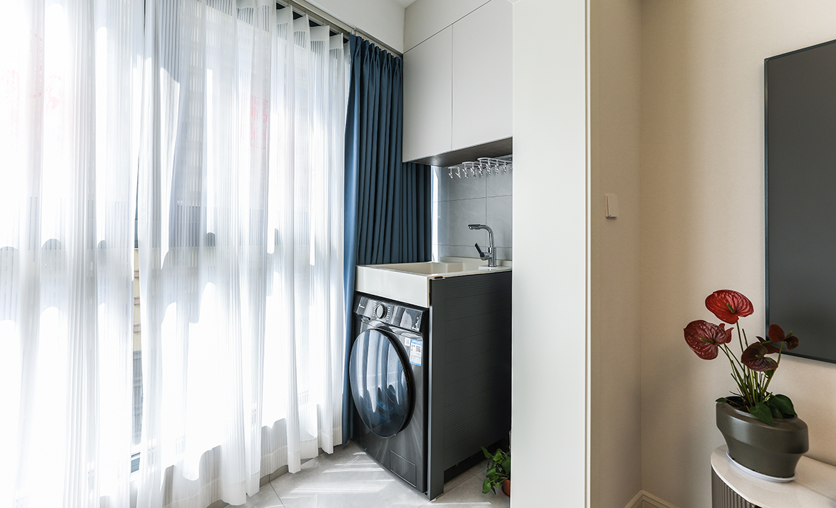 陽臺是晾曬衣物的場所，一側洗衣機和水池，一側為儲物柜，顏色以白色為主，儲物柜白色門板和門套相搭配，超大玻璃窗讓陽光柔和的照進來，很舒適、很愜意。