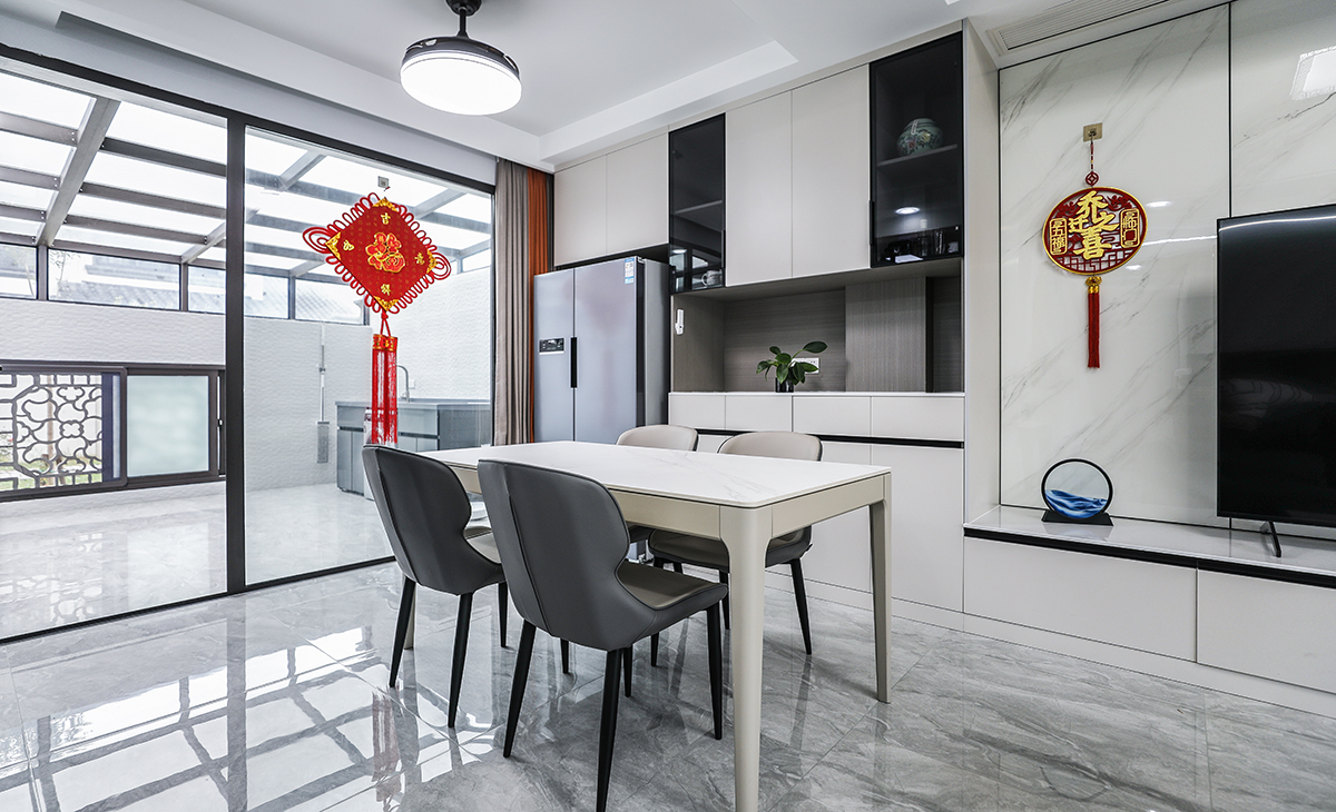 餐廳空間比較方正寬敞，又有一個大落地窗，靠墻做一排裝飾柜，既實用、又有裝飾功能，膚感灰+木色框架，極窄邊框玻璃門門板相呼應，巖板餐桌把用餐氛圍調和的很溫暖，淺灰色地磚很干凈，色彩和造型上都簡潔大氣。