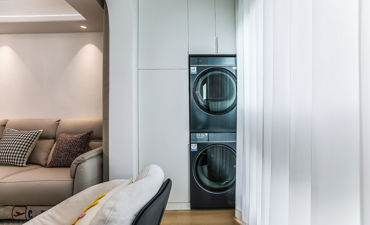 陽(yáng)臺(tái)是晾曬衣物的場(chǎng)所，洗衣機(jī)和烘干機(jī)疊放，一側(cè)為儲(chǔ)物柜，顏色以白色為主，超大玻璃窗讓陽(yáng)光柔和的照進(jìn)來(lái)，很舒適、很愜意。