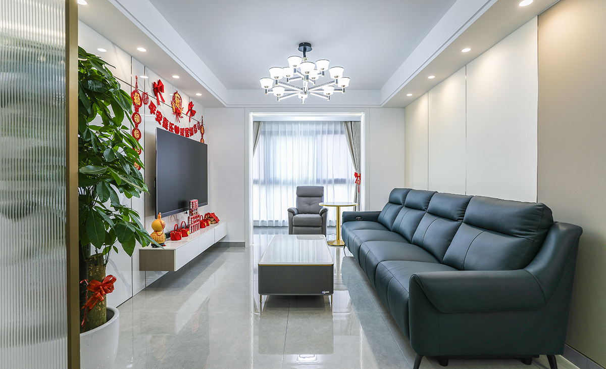 客廳開間很大，電視墻整體做石紋竹木纖維板，灰白色調的石紋和極窄線條，明暗有神，藏青色皮質沙發立刻檔次提高很多，放一組按摩沙發，客廳空間也很寬闊。吊頂造型上采用雙眼皮吊頂。地面采用淺灰色地磚。造型和色調上無不給人以簡潔、大氣、時尚的感覺。 