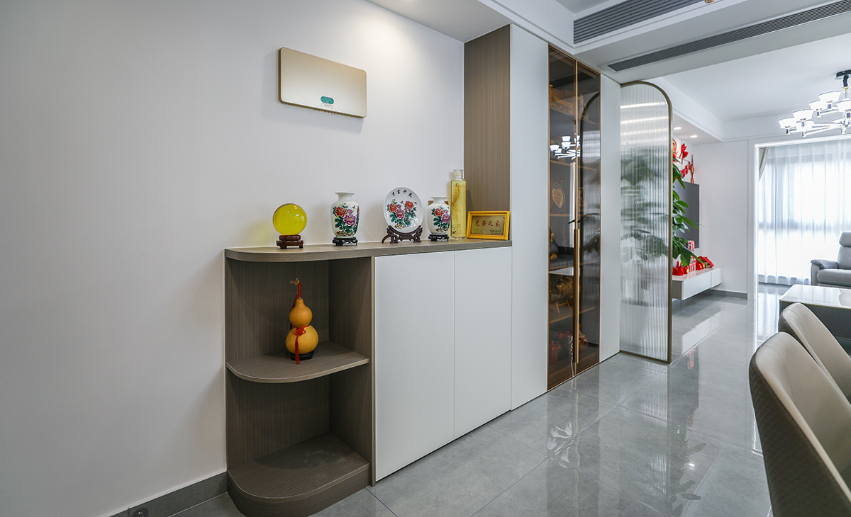 本套房子的進門玄關柜設計也是一大亮點，對外圓弧形角矮柜到內頂天立地四扇高柜，中間玻璃門，體現了主人生意人的處事圓潤，做人挺直腰桿心胸坦蕩，屏風采用金色弧形設計，和矮柜圓形角相呼應，給人感覺不僅雅致而且有韻味。