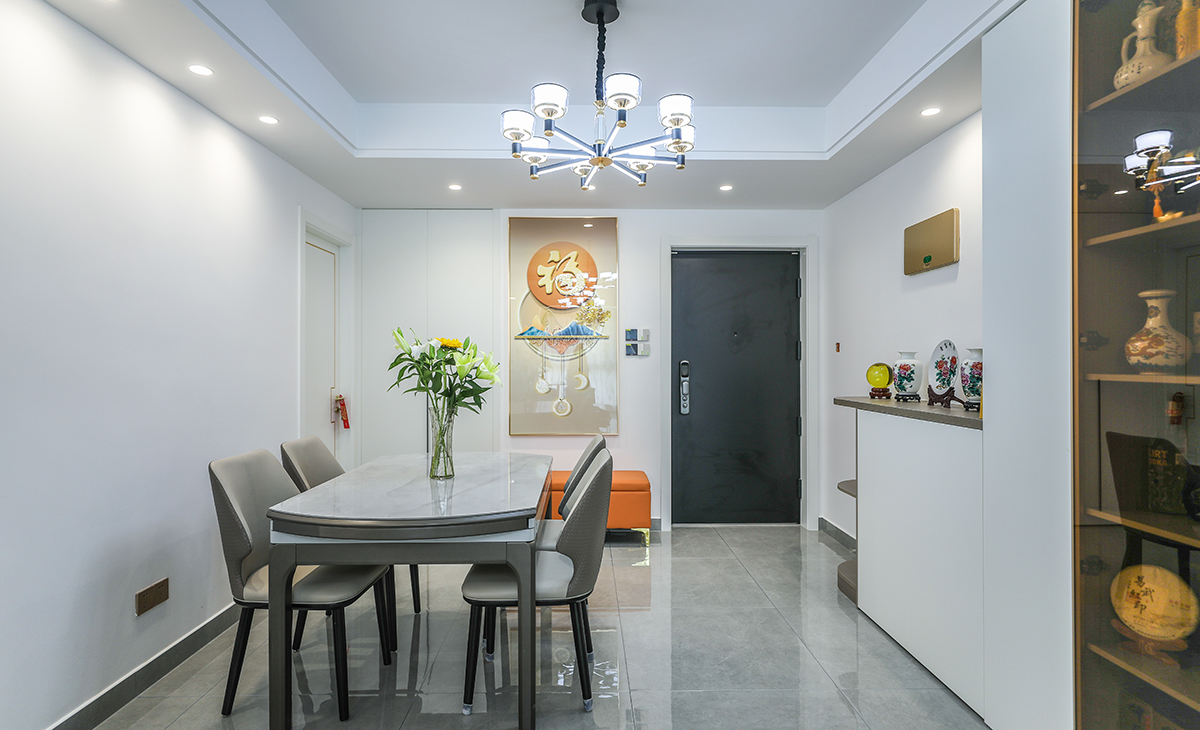 餐廳空間比較方正寬敞，進門右手邊是橙色換鞋凳，和裝飾畫遙相呼應，靠左墻做一排矮柜和酒柜，既實用、又有裝飾功能，原木色框架，極窄邊框玻璃門和白色木門板相呼應，巖板餐桌把用餐氛圍調和的很溫暖，淺灰色地磚很干凈，色彩和造型上都簡潔大氣。