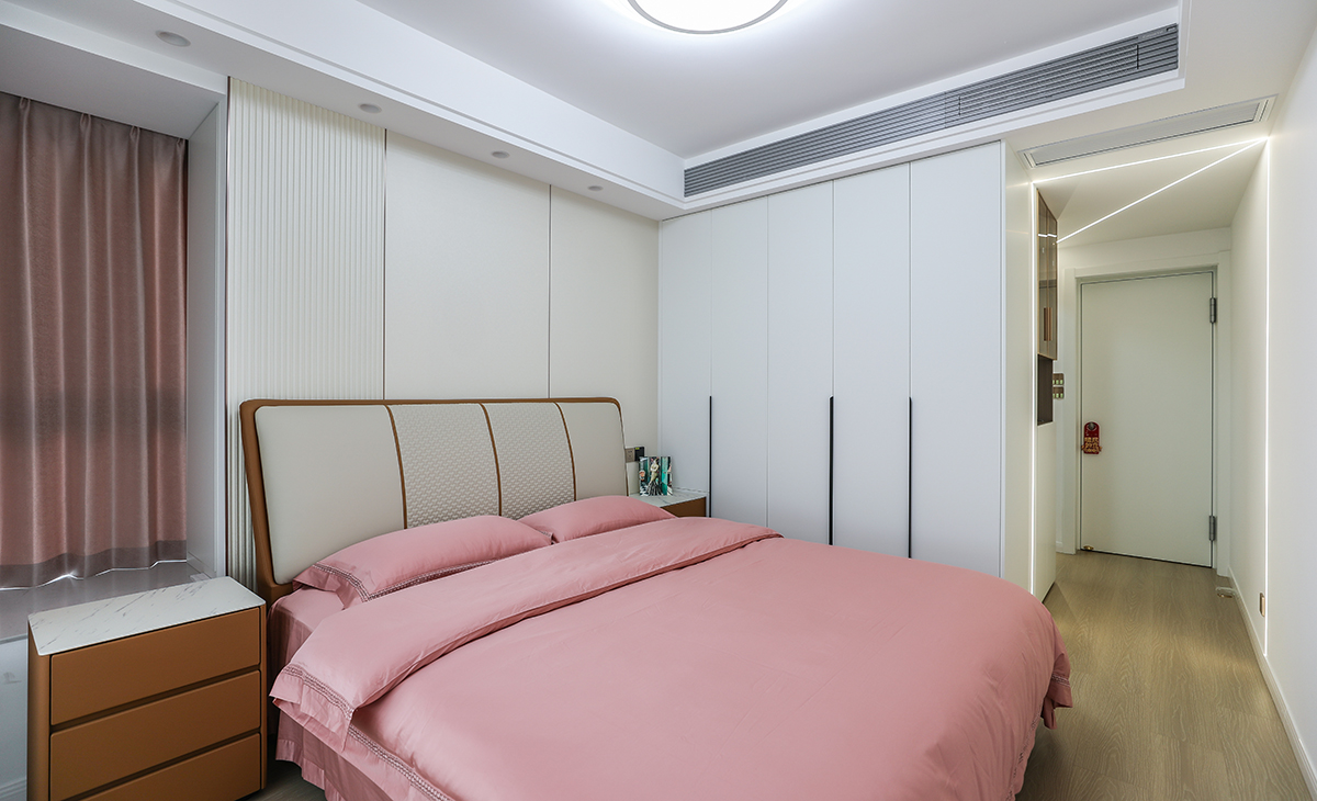 主臥奶白色床頭背景配上床的米色皮質靠背非常和諧，衣柜門板也是白色，和墻面融為一體，很自然，上方的通體空調風口，過道線性燈，體現了輕奢風格的貴氣、穩重，不單調。