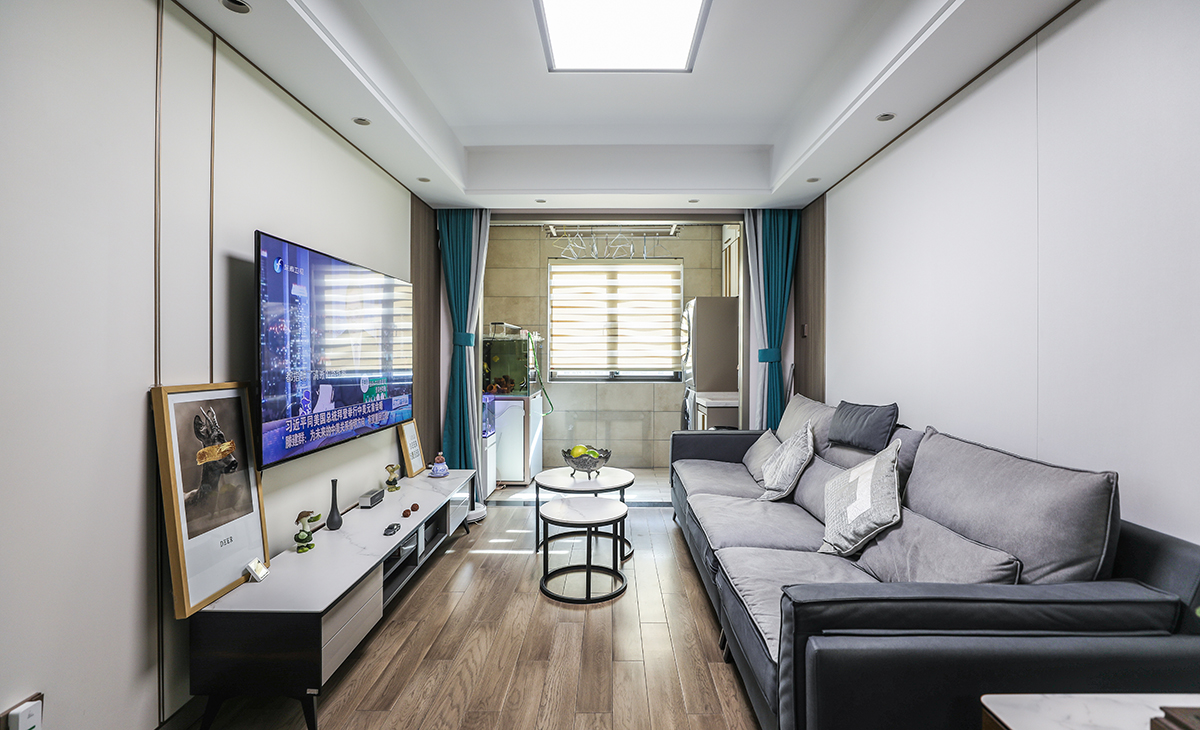 客廳開間不算太大，電視墻做纖維大板，用金屬線條做點(diǎn)綴，更顯簡單大氣，加上落地電視柜，75寸電視機(jī)掛墻，空間上也很寬裕。吊頂造型上采用雙眼皮吊頂。地面采用地板，整個客廳的溫馨感也提升一個層次。造型和色調(diào)上無不給人以簡潔、大氣、時尚的感覺。