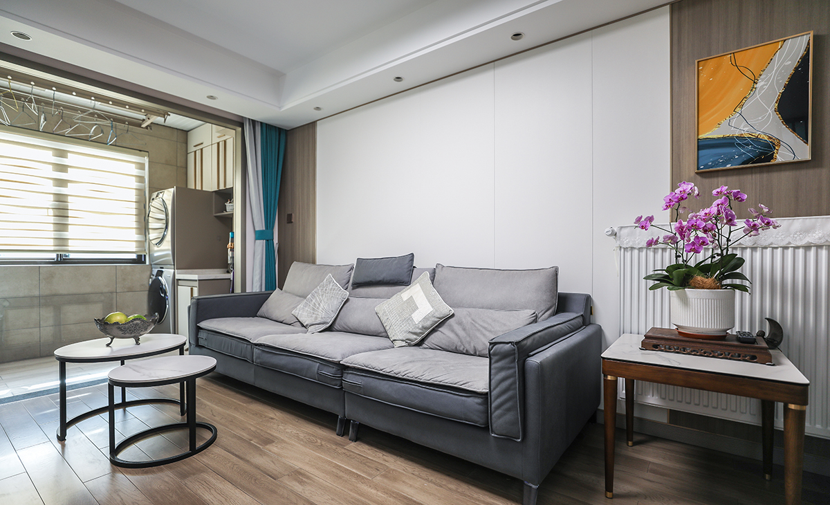 沙發(fā)背景墻也是采用纖維大板材質(zhì)，用純色和木色進(jìn)行簡單拼接，沙發(fā)邊放上一個邊幾，放置裝飾花瓶和掛畫，作為點(diǎn)綴，讓整個空間變得更加靈動。