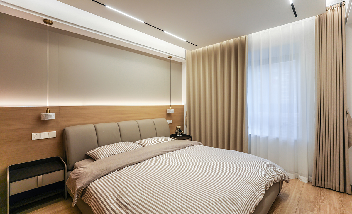 主臥地面鋪的實木復(fù)合地板，背景墻選了現(xiàn)在比較流行的硬包+原木色墻板，柔和的色調(diào)，半墻造型點綴燈帶線，讓家里氛圍感更純粹。皮革硬包+原木色木飾面+燈帶，見光不見燈，美觀又大方。頂上采用懸浮無主燈+線性燈，配上兩邊的吊燈，整個空間層次明細(xì)，整體效果突出，配上咖啡色的窗簾和白沙，更大氣，時尚。