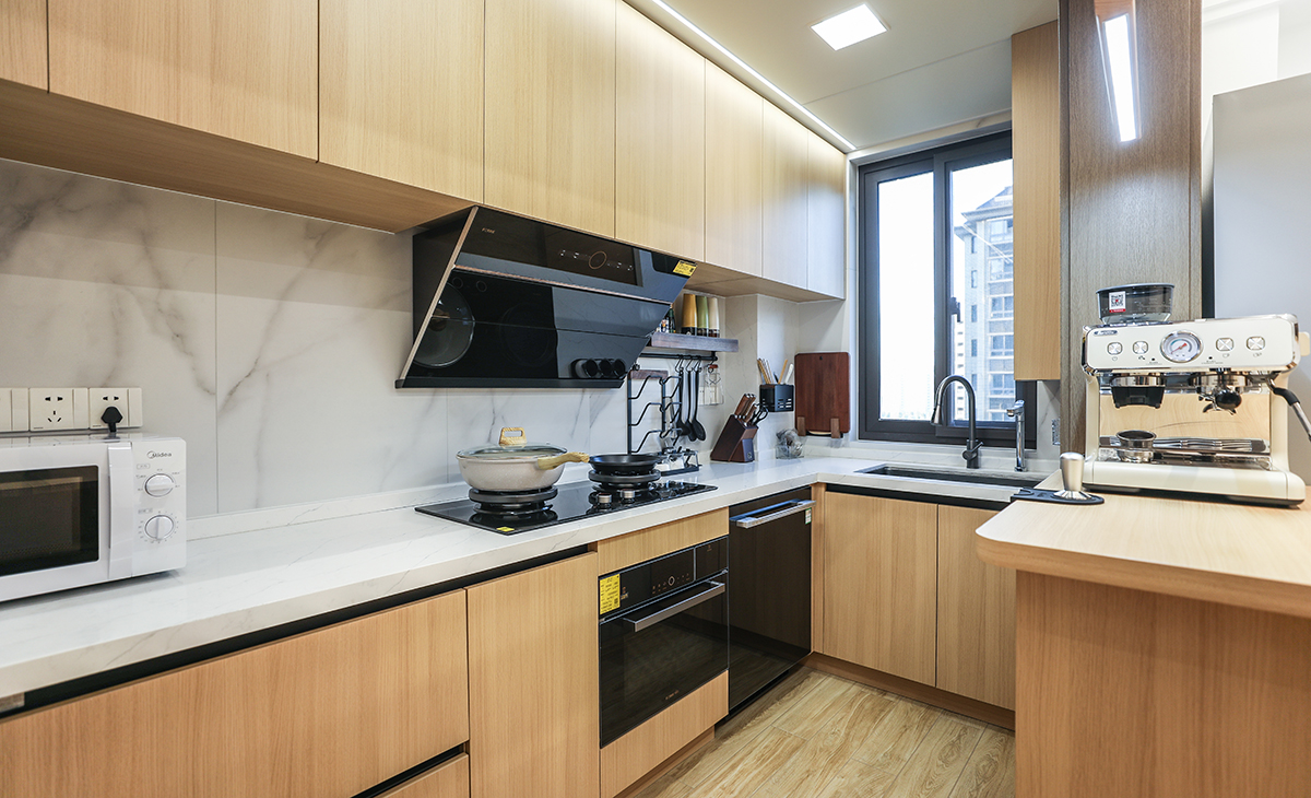 廚房間本來是長方形封閉式的空間，改成開放式的廚房，配上吧臺，L型櫥柜整體采用原木色門板，配上白色的臺面，整體干凈、簡潔，地面用的木紋磚，與廚柜門板和吧臺顏色統(tǒng)一，頂面采用現(xiàn)在流行的大板吊頂配上線性燈，時尚、溫馨。