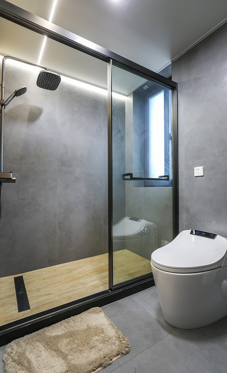 衛(wèi)生間地面鋪600*1200的啞光灰色地磚，直接拿地面磚上墻，整個空間更大氣、明亮，衛(wèi)生間濕區(qū)采用木紋磚，更干區(qū)的臺盆柜墻面顏色統(tǒng)一，地面選用的槍灰色地漏，頂面采用現(xiàn)在流行的蜂窩大板，再配上線性燈和筒燈，讓整個衛(wèi)生間更上檔次和溫馨。淋浴龍頭的位置，做了一個壁龕，分三層，可以平時作為收納功能使用，淋浴房、淋浴龍頭、地漏全部選擇一個顏色，整個顏色統(tǒng)一，更能凸顯原木風(fēng)。