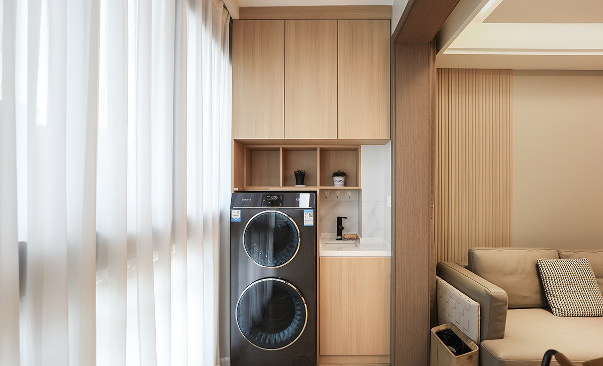 陽臺作為生活的晾曬衣物場所，它不僅有收納和洗衣服功能，整體空間設(shè)計好以后，效果更突出，也能作為觀賞的一處景物。原木色柜體和門板做了當(dāng)下很流行的洗衣柜組合，上面的收納柜和對面的儲物柜形成了鮮明的對比，長長的收納柜，既可以放吸塵器，又美觀簡約時尚，配上白色紗簾，把原木色的風(fēng)格，簡單明了的凸顯出來，既時尚又溫馨，達(dá)到了業(yè)主想要的美觀和實用并存的效果。