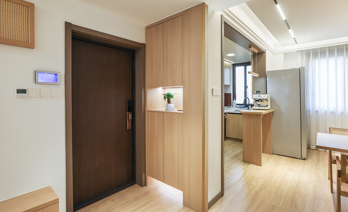 進(jìn)門口地面鋪的實木復(fù)合地板，左手邊做了原木色鞋凳，上面的配電箱也選擇了原木色的裝飾畫作為隱藏，右手邊做了一個收納鞋柜，中間和下面做鏤空，原木色的柜體和門板配上線性燈，更簡潔、明亮。