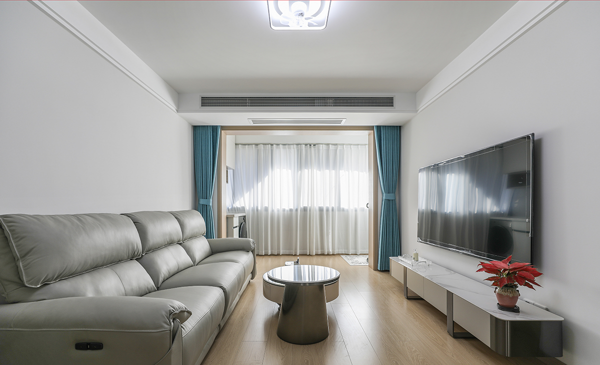 客廳開間很大，淺灰色皮質沙發立刻檔次提高很多，網紅茶幾，客廳空間也很寬闊。吊頂造型上采用雙眼皮吊頂。地面采用原木色地板。造型和色調上無不給人以簡潔、時尚的感覺。