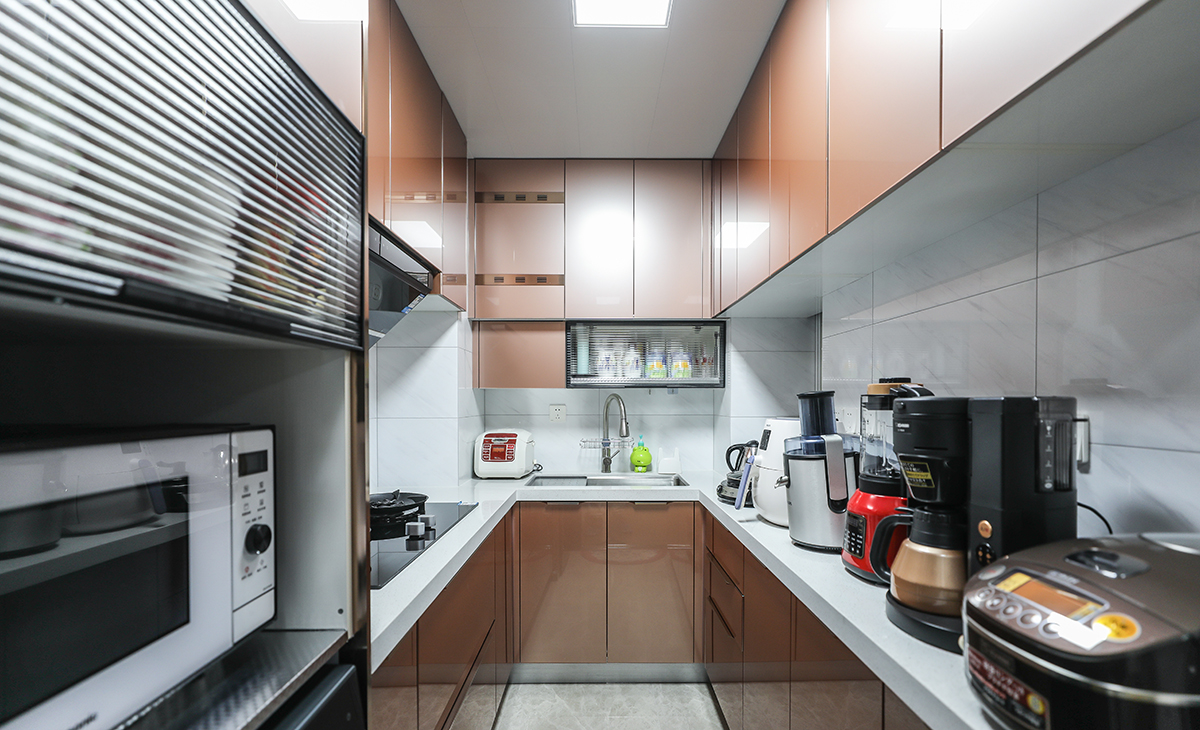 該套房子廚房設計U型櫥柜，增加操作臺面，一邊40cm深淺柜，用來放各種設備，顏色搭配合理統一，石英石材質臺面更好打理，滿足主人制作各種美食的需求，原櫥門拆除，做三聯玻璃移門，整體進出更加方便，空間顯明亮。