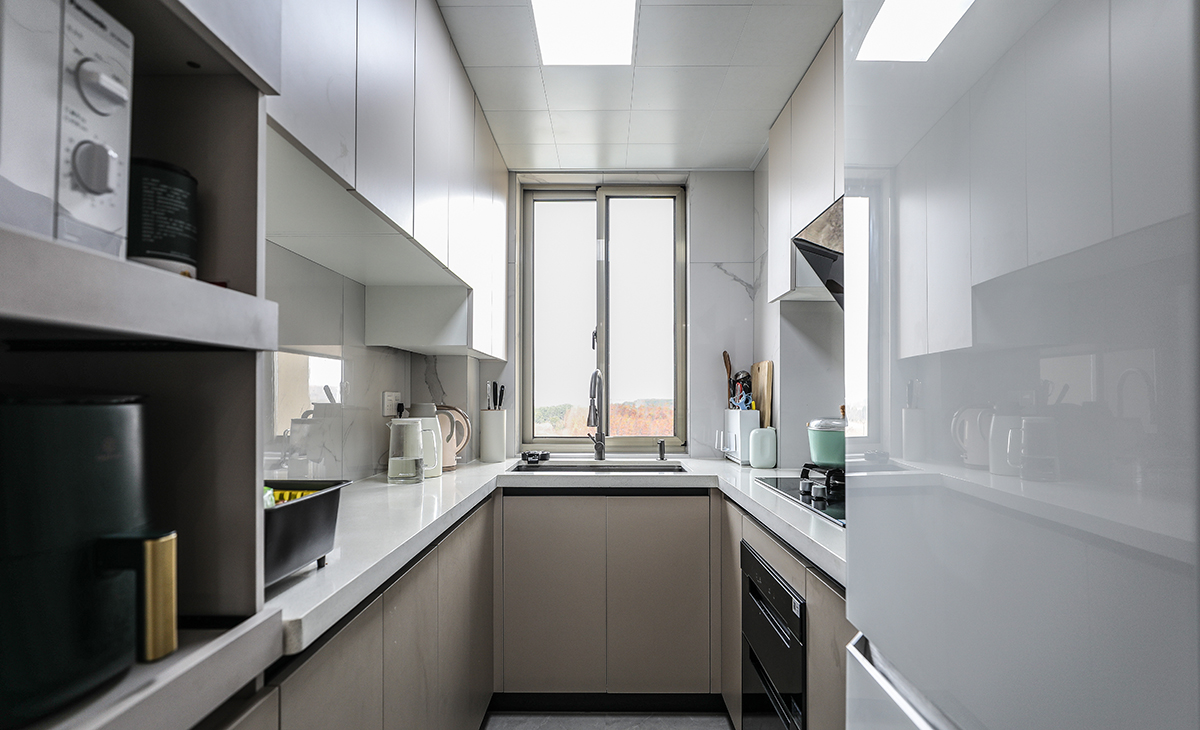 該套房子廚房設計U型櫥柜，增加操作臺面，一邊40cm深淺柜，用來放各種設備，顏色搭配上淺下深，石英石材質臺面更好打理，空間劃分合理，滿足主人制作各種美食的需求，原櫥門拆除，做三聯玻璃移門，整體進出更加方便，空間顯明亮。