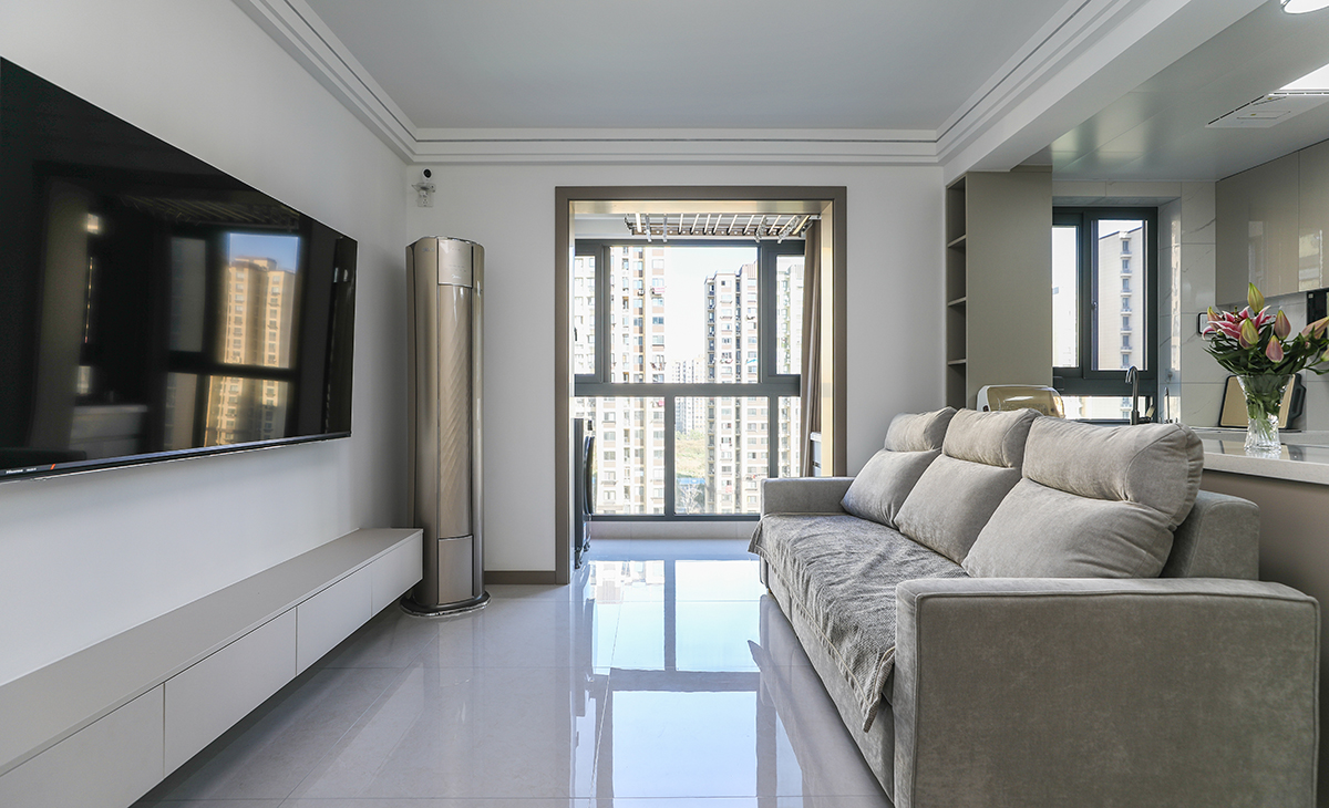 客廳開間很小，沙發靠背直接銜接廚房，增加客廳的通透性，視覺更加通透，明暗有神，淺灰色沙發立刻檔次提高很多，客廳空間也很寬闊。吊頂造型上采用雙眼皮吊頂。地面采用淺灰色地磚。造型和色調上無不給人以簡潔、大氣、時尚的感覺。
