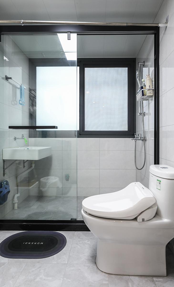 衛生間設計風格簡約而時尚，整體色調以白色和灰色為主，給人一種清新整潔的感覺。墻磚采用淺灰色，與白色馬桶和洗手臺相得益彰，增強了空間的層次感。