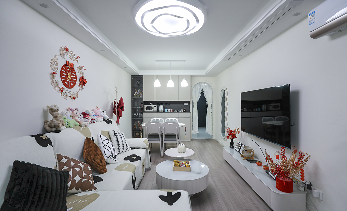 客廳開間較長，平時(shí)用電視機(jī)，周末休息時(shí)可以用投影在家里就能體驗(yàn)影院般的效果，空間也很寬闊、裝飾柜采用淺灰色門板，墻面用暖白涂料增加亮度，吊頂造型上采用雙眼皮吊頂。地面采用淺灰木色地板。造型和色調(diào)上無不給人以簡潔、大氣、時(shí)尚的感覺。