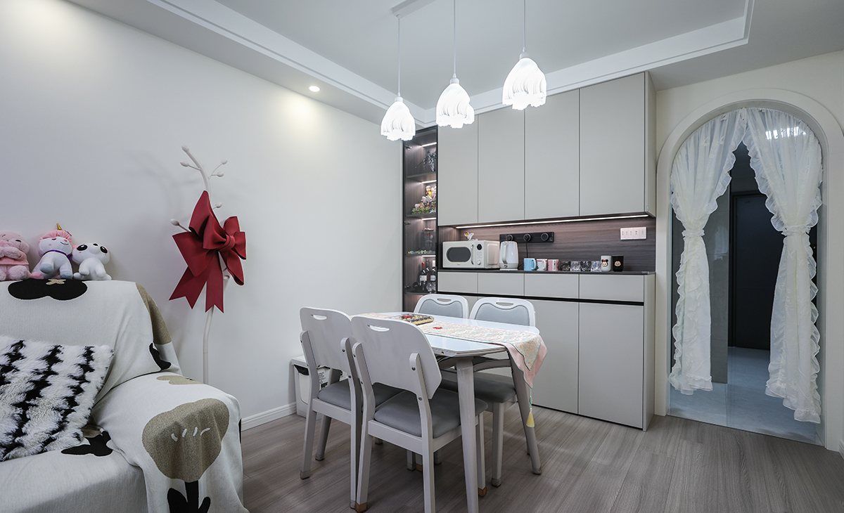 餐廳餐桌搭配餐邊柜，既實(shí)用、又有裝飾功能，頂上小吊燈增加氛圍感，玻璃柜和鏤空柜放置燈帶，使空間更加飽滿，巖板餐桌把用餐硬度高又好打理，放油抗污，地面同客廳地板通鋪，整體色彩和造型上都簡潔大氣。