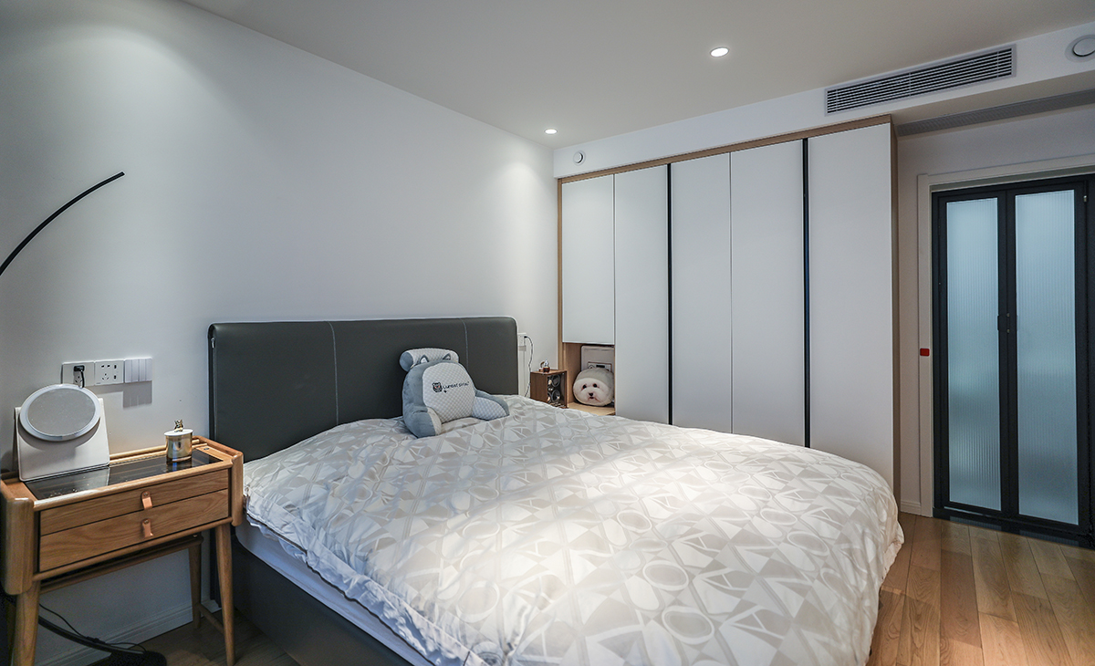 主臥也是無主燈的設計，主打就是簡潔，地面原木地板，床選擇了灰色的皮床，簡單的原木床頭柜，空間非常溫馨。