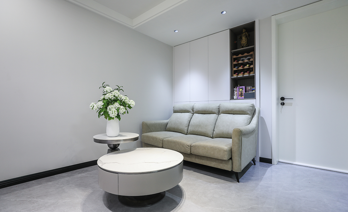 沙發背景上吊嵌入式壁柜，白色的門板配備深灰色開放隔顏色相輔相成，因客戶家為一樓光線較暗，色調上墻面涂料全部采用白色乳膠漆，沙發用淺灰色，深淺搭配的錯落有致，既溫馨又簡潔。