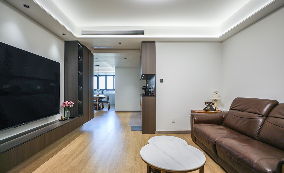 客廳是接待客人的空間、是家庭裝修的亮點所在、也是一家人活動頻率最高的區域，棕色皮質沙發，體現穩重大氣，吊頂造型上采用方形石膏板+燈帶，時尚氣息很濃。地板采用淺色原木色，電視柜和組合柜都漏空，方便清潔。造型和色調上無不給人以簡潔、大氣、時尚的感覺。