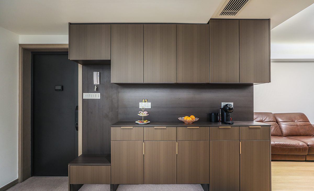  本套房子的玄關設計也有巧妙之處，進門左邊一整面墻都做了鞋柜、換鞋凳，高低錯落有致，一方面具有裝飾的功能，另一方面又具有儲物的功能，深色柜子和防盜門相搭配，讓整個空間在視覺上既協調又統一。