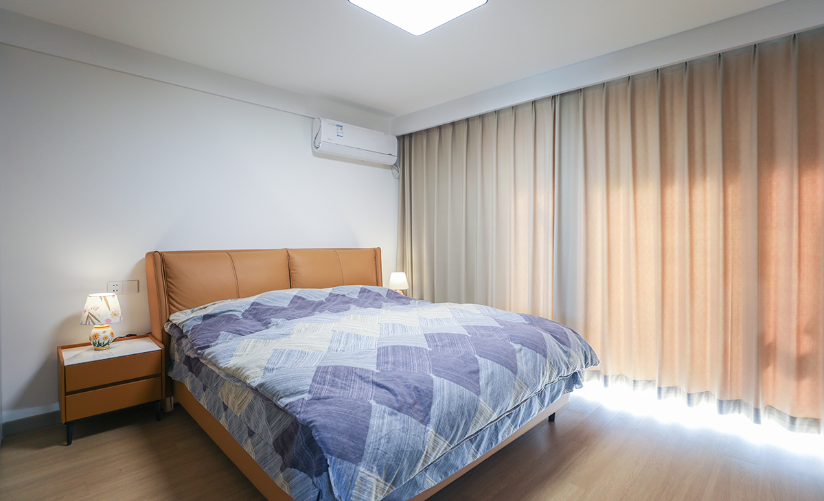 主臥一整面淺粉色窗簾，陽光若隱若現的透進來，原來是有梁和斜墻亂成一體的空間，但經過設計師的手筆改造，把整個空間變成具有儲物和居住功能，又有線條感的優美空間。