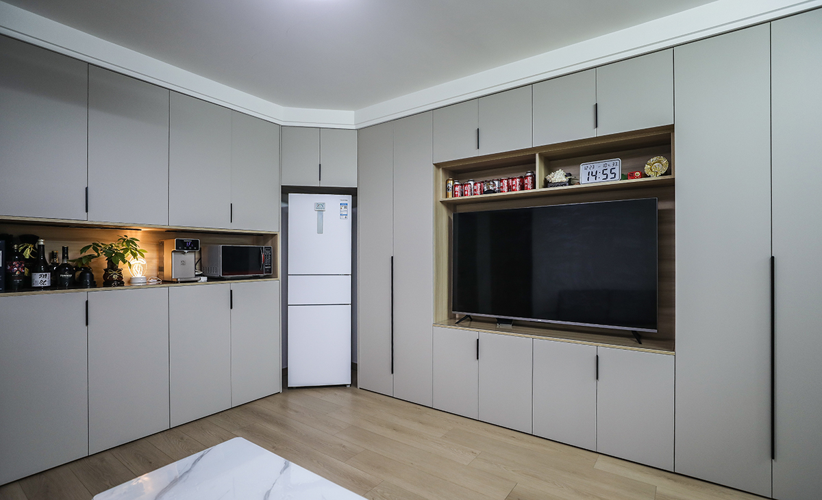  本套房子的客廳儲物柜設計是一大亮點，既實用，又有裝飾性，上下儲物柜，中間留鏤空，展示主人收藏的藝術品，門板采用平板一門到頂，和臥室門顏色相統一，給人感覺不僅雅致而且有韻味。