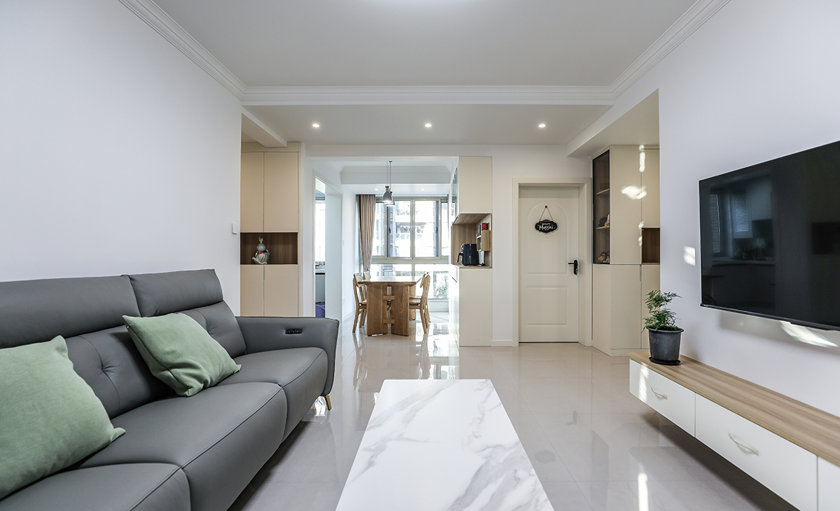 客廳開間較長，80寸電視機在家里就能體驗影院般的效果，空間也很寬闊、裝飾柜采用暖白色門板，增加亮度，吊頂造型上采用石膏線。地面采用亮光淺色地磚。造型和色調上無不給人以簡潔、大氣、溫馨的感覺。