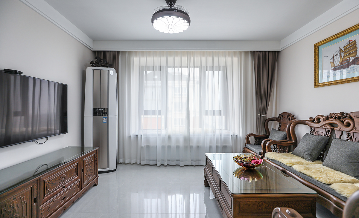  客廳開間很大，客戶家里實木家具是原先保留下來的，雞翅木質感強硬，跟客戶雍容華貴的身份相吻合。客廳空間也很寬闊。吊頂造型上采用雙眼皮吊頂。地面采用淺灰色地磚。造型和色調上無不給人以簡潔、大氣、時尚的感覺。