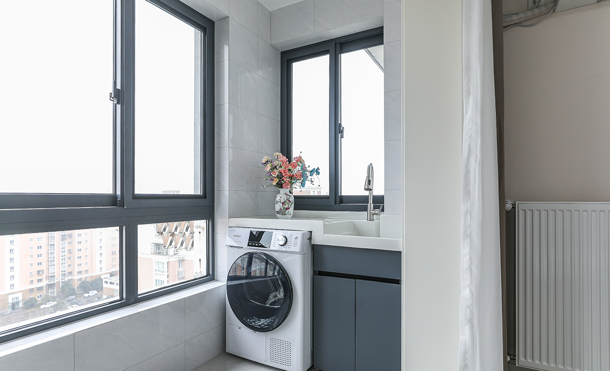 陽臺是晾曬衣物的場所，一側烘干機和水池，一側為儲物柜，顏色以白色為主，儲物柜白色門板和門套相搭配，超大玻璃窗讓陽光柔和的照進來，很舒適、很愜意。