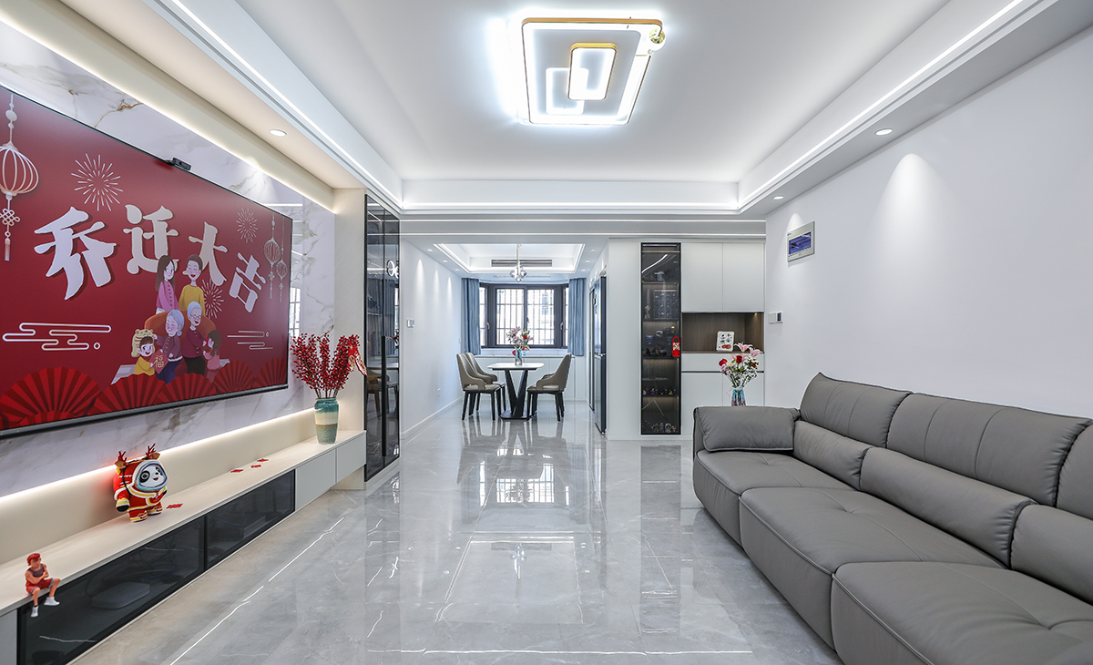  客廳開間很大，電視墻做了巖板與木飾格柵，淺的巖板和原木色木飾面相互配合，明暗有神，深灰色皮質沙發立刻檔次提高很多，客廳空間也很寬闊。吊頂造型上采用雙眼皮加線性燈組合吊頂。地面采用淺灰色地磚。造型和色調上無不給人以簡潔、大氣、時尚的感覺。