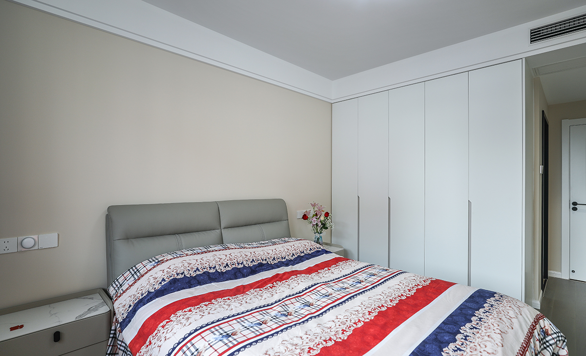 主臥地面采用的是實木復合地板淺灰色，與床及床頭柜搭配為一體，更衣柜采用一門到頂做法，預留暗裝拉手造型以簡潔平板為主，方便打理，頂面為雙眼皮吊頂，內嵌中央空調，在每個角度我們臥室都是一個整潔、簡約、也不失優雅的一個空間。