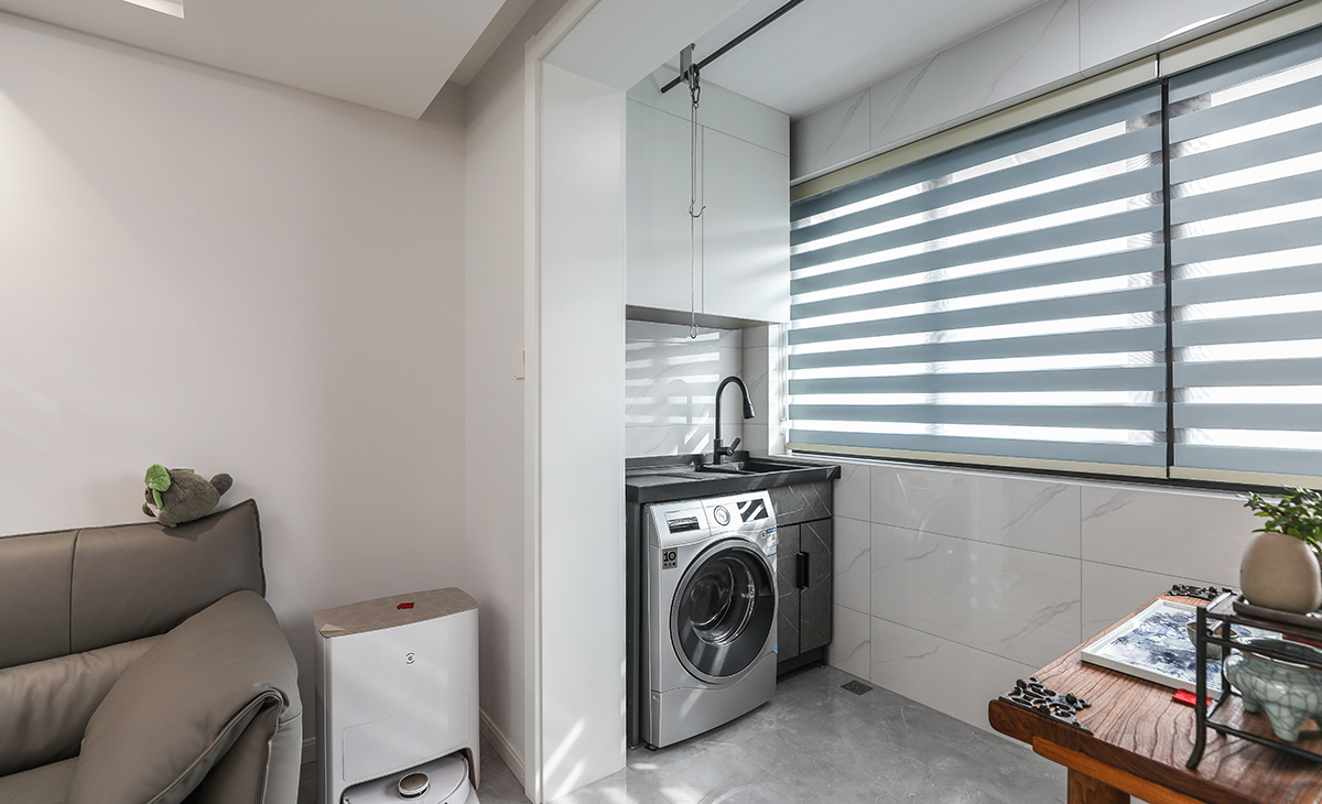 陽臺是晾曬衣物的場所，一側洗衣機和水池，一側為喝茶區，顏色以原木為主，彰顯主人生活品味，超大玻璃窗讓陽光柔和的照進來，很舒適、很愜意。