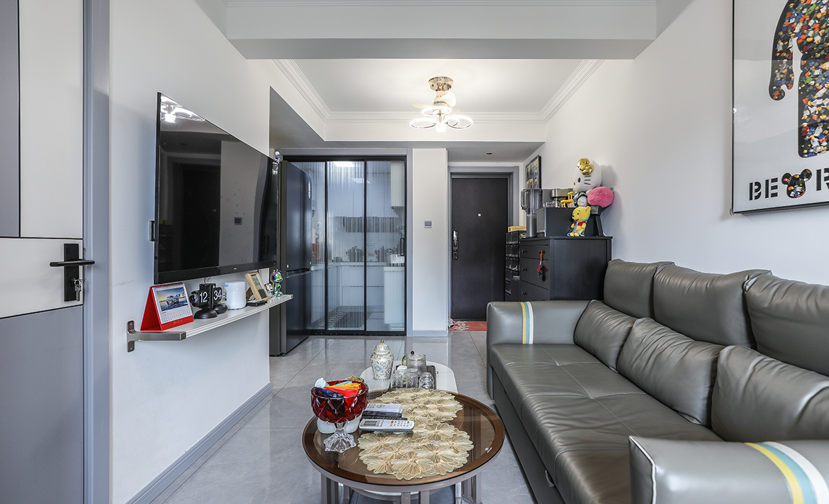 客廳開間很小，電視墻很簡單，直接掛墻電視，沙發背景淺灰色涂料相互配合，明暗有神，深灰色皮質沙發立刻檔次提高很多，客廳空間也很寬闊。吊頂造型上采用雙眼皮吊頂。地面采用淺灰色地磚。造型和色調上無不給人以簡潔、大氣、時尚的感覺。