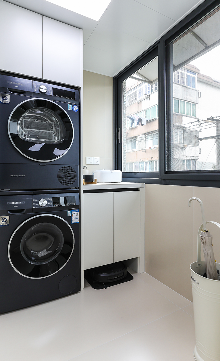 北陽臺是晾曬衣物的場所，一側洗衣機和水池，上方為儲物柜，顏色以米白色為主，儲物柜米色門板和門套相配，大玻璃窗讓陽光柔和的照進來，很舒適、很愜意。