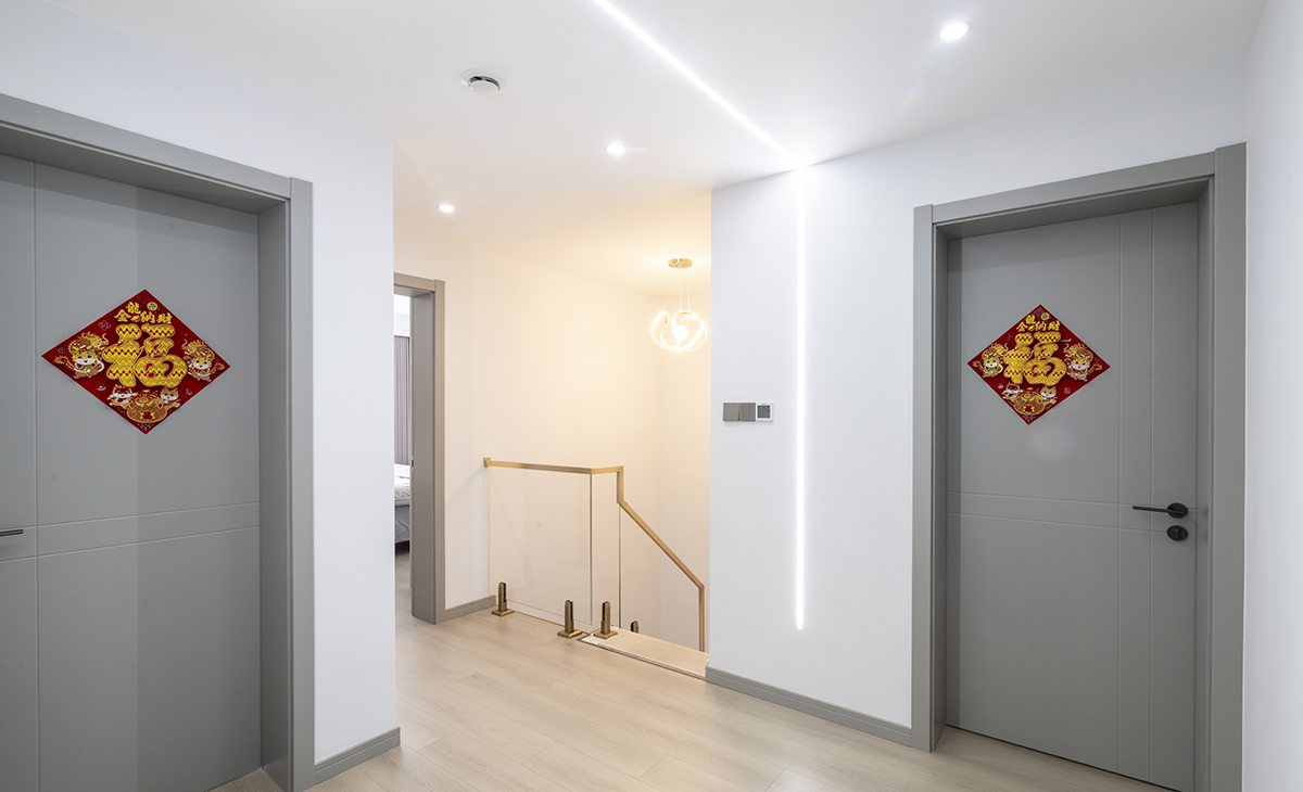 樓梯上來就是休閑區(qū)，采用無主燈設(shè)計，墻面和頂面的倒U字型線燈，讓空間豐富起來，白色墻面和灰色木門搭配，光線明亮通透，顏色搭配明暗有序。