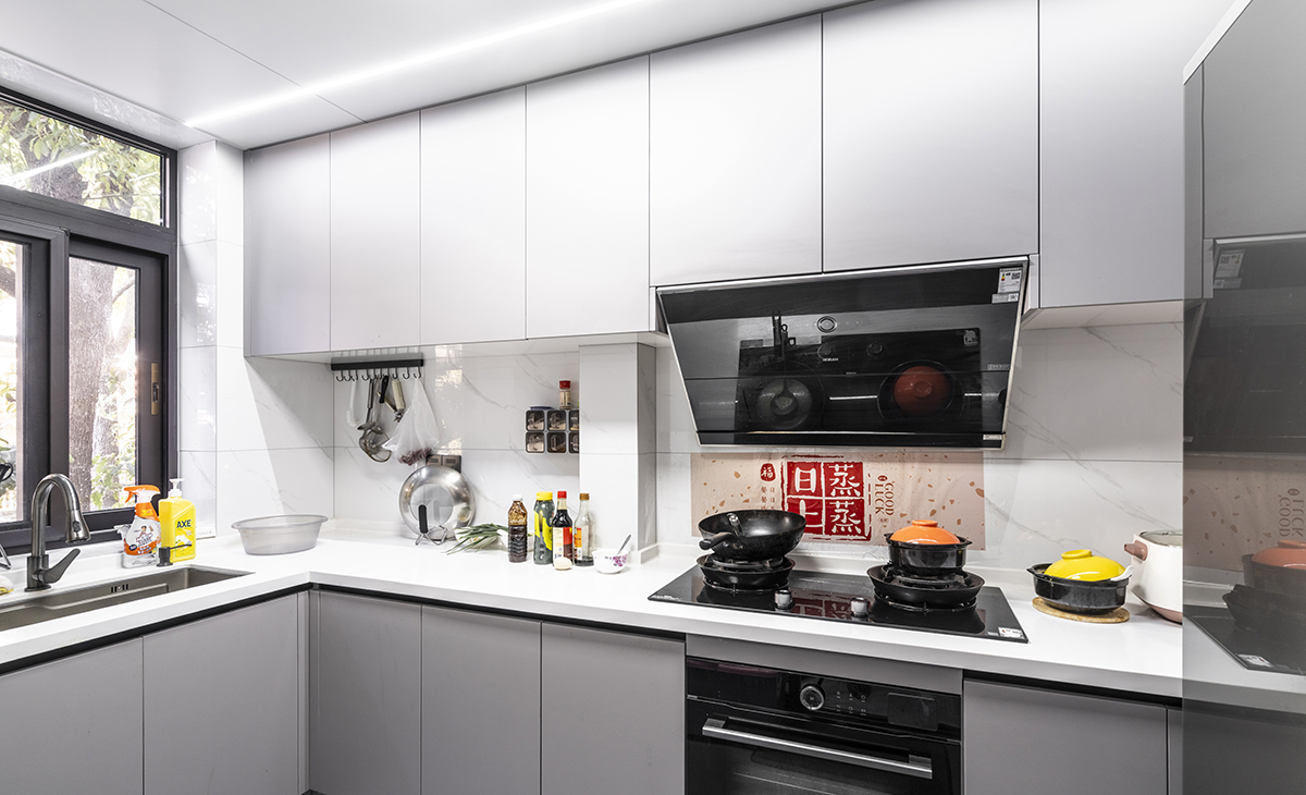 該套房子廚房空間很大，做成L型櫥柜，蒸烤一體機放煤氣灶下面，上柜淺灰、下柜深灰，臺面白色，方便打理，大雙門冰箱滿足儲物空間。
