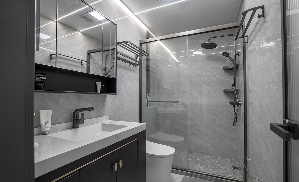 衛(wèi)生間采用灰色墻磚配胡桃木色浴室柜和白色石英石臺面，顏色明暗有序，從深到淺，色調(diào)很豐富，掛墻臺盆柜，墻排水設(shè)計，下方又設(shè)計一個地漏，顏色協(xié)調(diào)統(tǒng)一，主人很滿意，不斷地夸贊設(shè)計師對色彩的精準(zhǔn)把握。